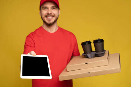 Happy delivery man with tablet in studio isolated yellow background.の写真素材