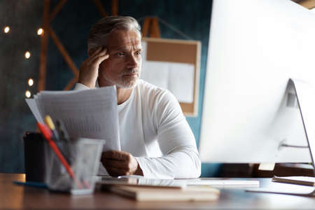 Casual Grey-haired businessman looking through paper documents. Male accounting manager reviewing financial reportの写真素材