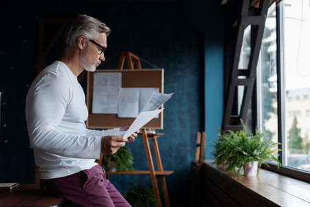 Casual Grey-haired Mature man reading paper in his office.の写真素材