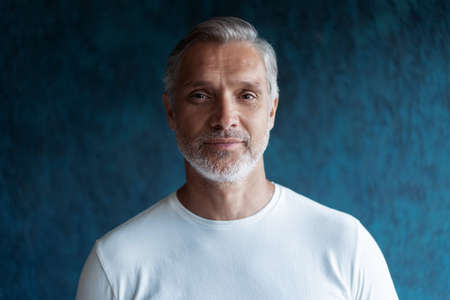 Casual Grey-haired Mature handsome man portrait over dark blue wall background.