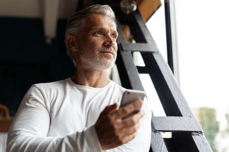 Business lifestyle. Casual Grey-haired Mature professional handsome businessman standing near window...