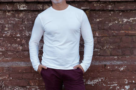 Portrait of a Grey-haired Mature handsome man in jeans and white t-shirt leaning to the old wallの写真素材