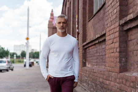 Portrait of a Grey-haired Mature handsome man in jeans and white t-shirt leaning to the old wallの写真素材