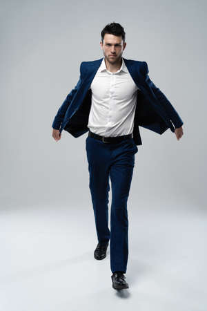 Perfect suit. Full length of handsome young man in suit looking at camera while walking against gray backgroundの写真素材