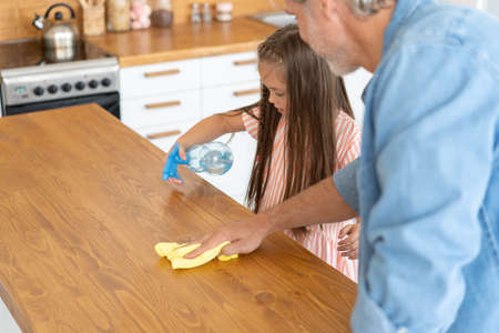 Cleaning time. Grey-haired Mature handsome man cleaning kitchen with daughter at the weekend.