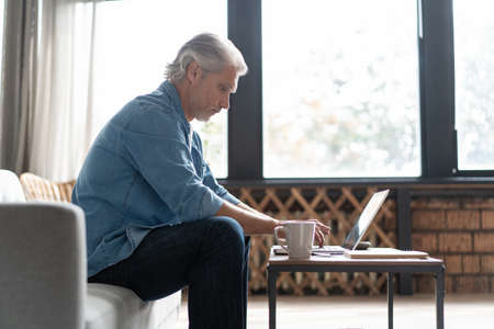 Middle-aged man working from home-office on laptop.の写真素材