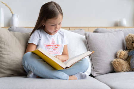 Young girl reading book at home. Distance education, home education. Self isolation concept.の写真素材