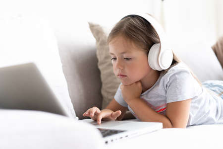 Online education. Sweet girl with headphones looking video lesson teacher conference laptop sitting on the couch at homeの写真素材