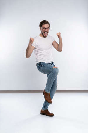 Happy winner. Happy young handsome man gesturing and keeping mouth open while standing against white background.の写真素材