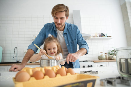 Caring young Caucasian father and cute little preschooler daughter bake in kitchen at home togetherの写真素材