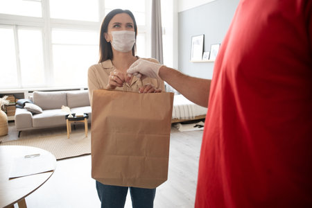 Postman or deliveryman paper package deliver to young woman customer in front of door at homeの写真素材