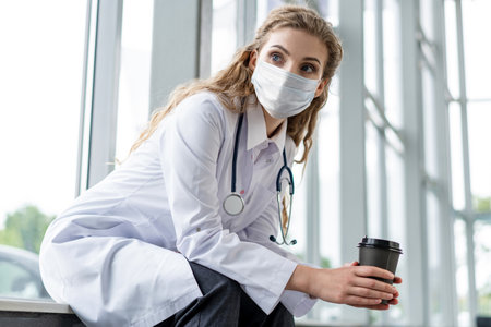 Portrait of tired exhausted nurse or doctor in face mask having a coffee break in hospital.の写真素材