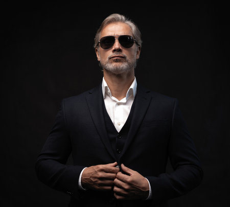 Portrait of a respectable mature man in a suit and sunglasses on a black background. Businessman portrait. Copy spaceの写真素材