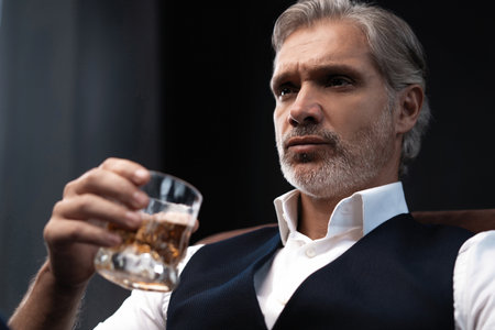 Portrait of handsome elegant mature man with a glass whiskey in a dark room.の写真素材
