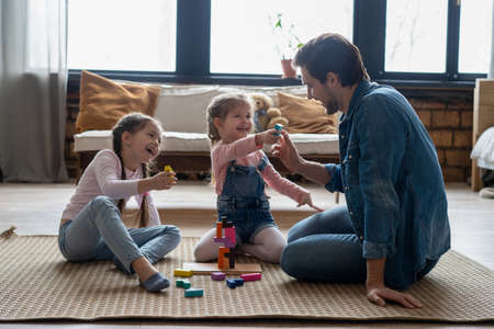 Loving young father lying on floor with small kids have fun engaged in funny activity with construction bricksの写真素材