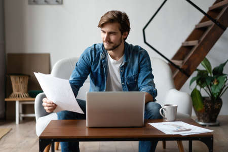 Entrepreneur working with a laptop and holding a document in a little office or homeの写真素材