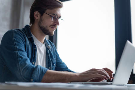 Successful entrepreneur smiling in satisfaction as he checks information on his laptop computer...