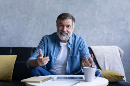 Happy senior retired man blogger looking at camera recording vlog, webcamera view portraitの写真素材