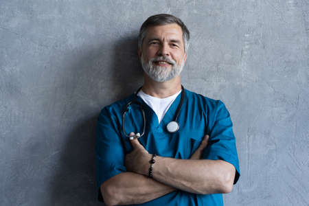 Portrait of professional mature surgeon looking at camera while standing against the grey background.の写真素材