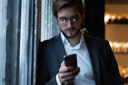 Handsome young man using smart phone during night. Closeup face of businessman messaging on cellphone at night in cafe.の写真素材