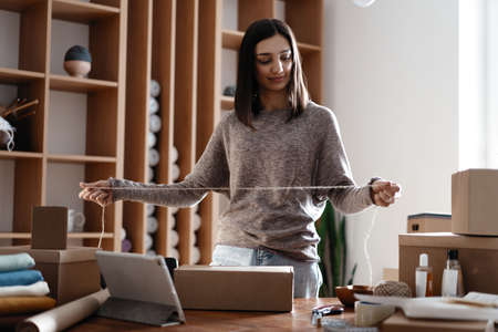 Indian mixed-race female business owner working, packing the order for shipping to customer