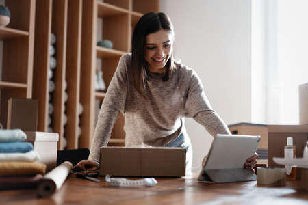 Indian mixed-race female seller using tablet checking ecommerce clothing store orders