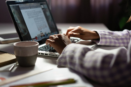 Woman uses a laptop while working on a new project idea late evening. Female hands are typing on...
