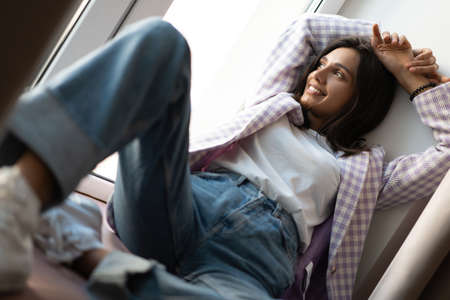 Young Indian mixed-race woman dressed casually sitting on the window sill at home officeの写真素材