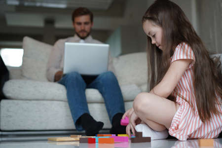 freelance and fatherhood concept - father working on laptop while daughter playing on the floor at...