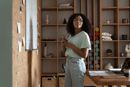 Focused young millennial african american woman in a casual clothes writes on the flip chart in the...