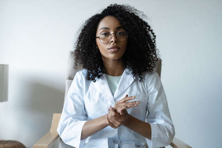 Mixed race woman doctor talking online with patient, making video call, looking at cameraの写真素材