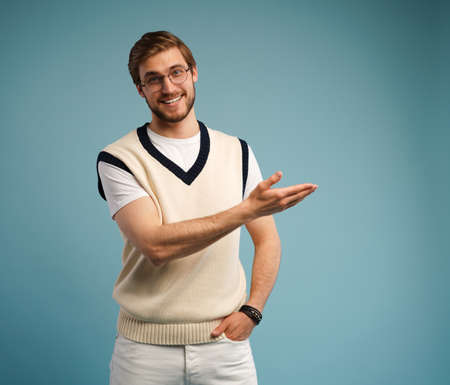 Portrait of a happy young man in casual pointing fingers away at copy space isolated over blue...