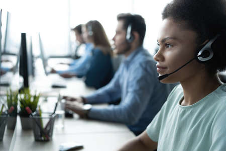 How can I help you? Beautiful call center workers in headphones are working at modern officeの写真素材
