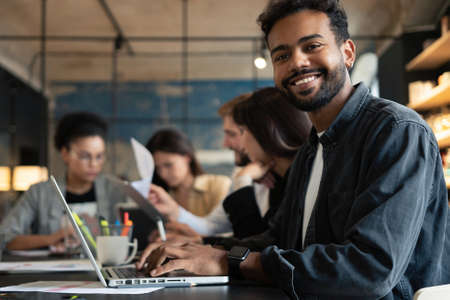 Portrait of confident mixed-race businessman sitting against colleagues in meeting room at office.