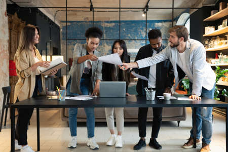 Group of young multiracial people in casual discussing strategy plan of collaboration standing at table in modern officeの写真素材