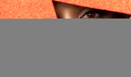 Face of a young beautiful girl with a bright make-up and with plump red lips peeks into a hole in shiny red paper.の写真素材