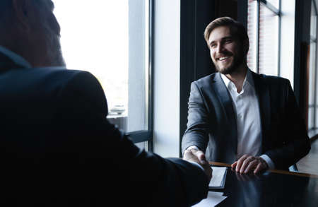 Good deal. Two business people shaking hands while sitting at the working place.の写真素材