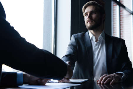 Good deal. Two business people shaking hands while sitting at the working place.の写真素材