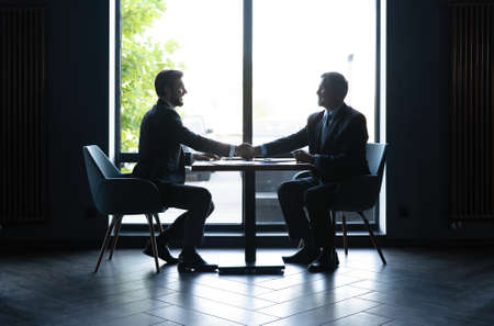 Good deal. Two business people shaking hands while sitting at the working place.の写真素材