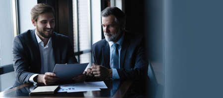 Senior and junior businessman discuss something during their meeting, office background.