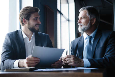 Senior and junior businessman discuss something during their meeting, office background.の写真素材