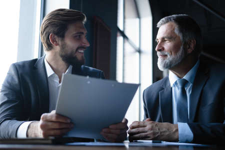 Senior and junior businessman discuss something during their meeting, office background.