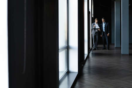 Two colleagues communicating in corridor, partners walking in the modern office