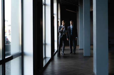 Two colleagues communicating in corridor, partners walking in the modern officeの写真素材