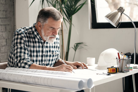 Mature Architect Engineer Design Working Planning Concept. Portrait of a smiling businessman working on blueprints at the officeの写真素材