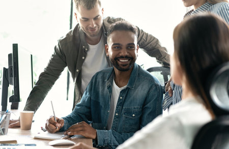 Friendly creative diverse colleagues team discuss online project use computer at workplace