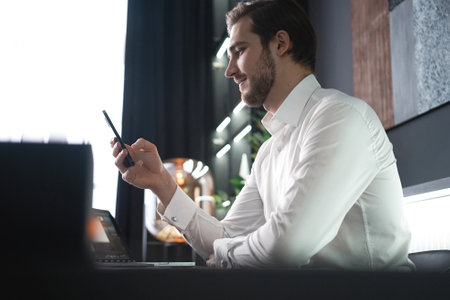 Smiling businessman holding smartphone sitting in office. Middle aged manager ceo using cell phone mobile apps. Digital technology applications and solutions for business developmentの写真素材