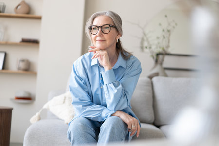 Happy mature woman relaxing on her couch at home in the living room. Portrait of happy woman in blue shirt smiling.の写真素材