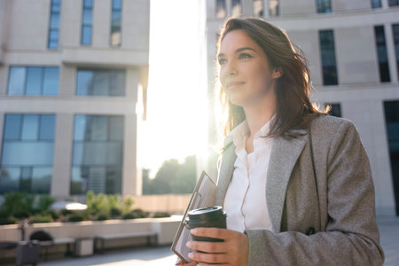 Beautiful Woman Going To Work With Coffee Standing Near Office Building. Portrait Of Successful Business Woman Holding Cup Of Hot Drinkの写真素材
