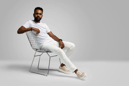 Handsome young african american guy sitting on stool, posing in studio - isolated.の写真素材